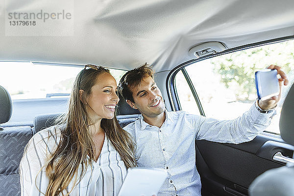 Lächelndes Paar auf dem Rücksitz eines Autos  das ein Selfie nimmt