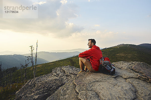 Mann sitzt auf einem Felsen und genießt die Aussicht während einer Wanderung