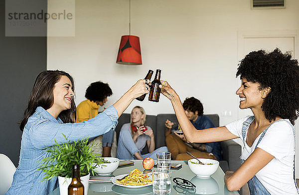 Lächelnde Freunde klirren mit Bierflaschen am Esstisch