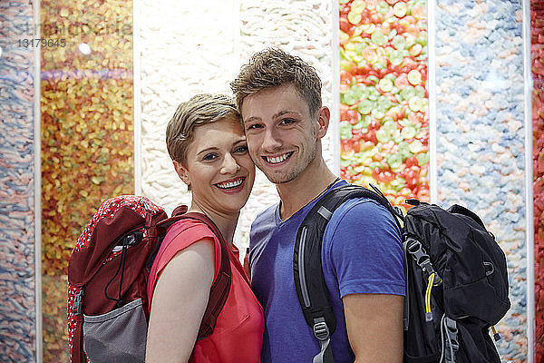 Porträt eines glücklichen Paares mit Rucksäcken an mehrfarbiger Wand