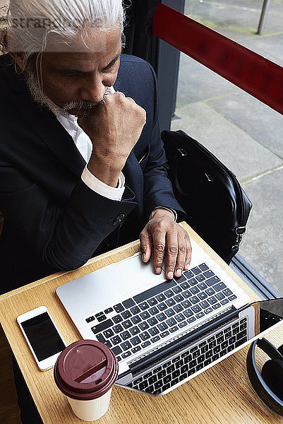 Leitender Geschäftsmann arbeitet am Laptop in einem Café