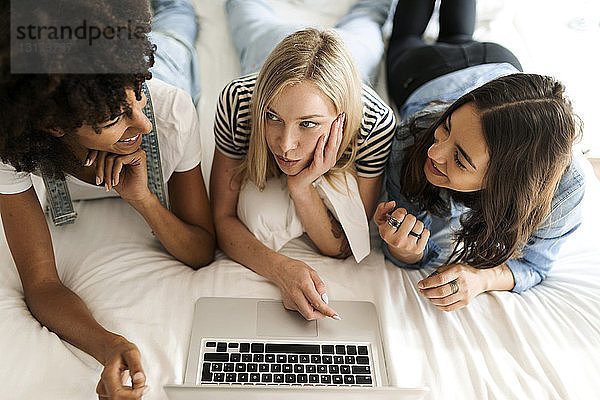Drei Freundinnen liegen im Bett und teilen sich einen Laptop