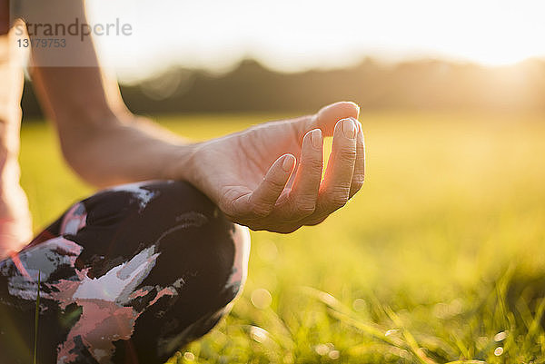 Detail einer Frau in Lotus-Position auf einer ländlichen Wiese bei Sonnenuntergang