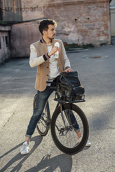 Junger Mann mit Pendler-Fixie-Fahrrad macht auf einem Hinterhof in der Stadt eine Pause