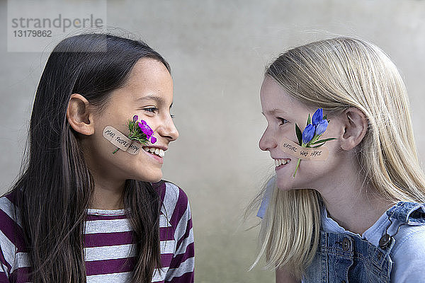 Zwei lächelnde Mädchen mit Blumenköpfen auf den Wangen