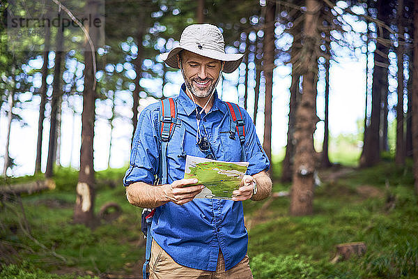 Lächelnder Mann schaut während einer Wanderung im Wald auf die Karte