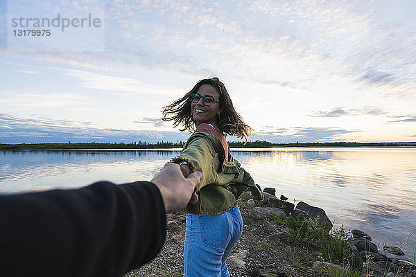 Finnland  Lappland  glückliche junge Frau  die in der Dämmerung am Seeufer die Hand eines Mannes hält