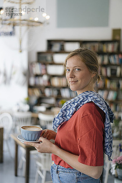 Porträt einer lächelnden jungen Frau  die in einem Café Kaffee serviert