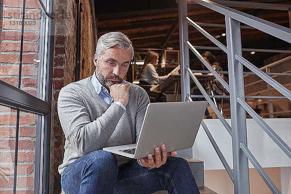 Geschäftsmann sitzt auf der Treppe eines modernen Büros und benutzt einen Laptop