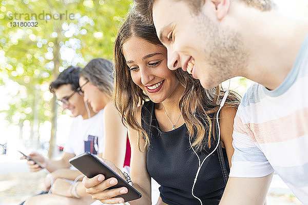 Eine Gruppe von Freunden in einem Park  die gemeinsam Spaß haben und Musik über Mobiltelefone hören