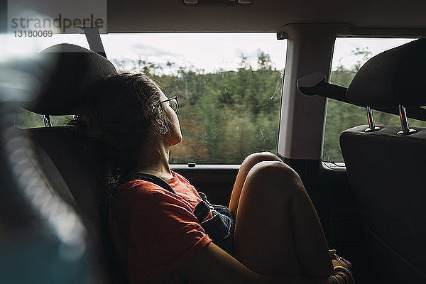 Junge Frau sitzt auf der Rückbank eines Lieferwagens  schaut aus dem Fenster und reist durch Norwegen