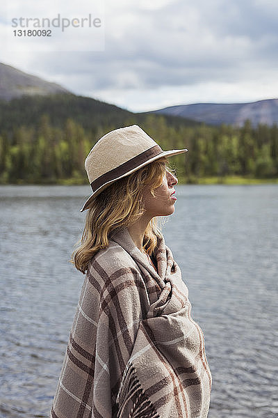 Finnland  Lappland  am Seeufer stehende Frau mit einem Hut  der in eine Decke gehüllt ist