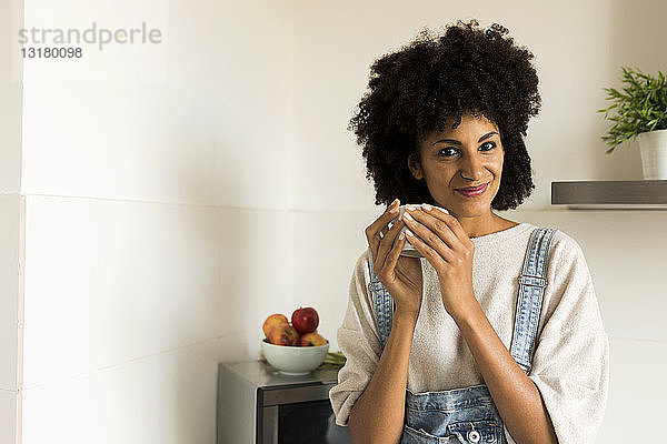 Porträt einer lächelnden Frau  die zu Hause in der Küche eine Tasse hält