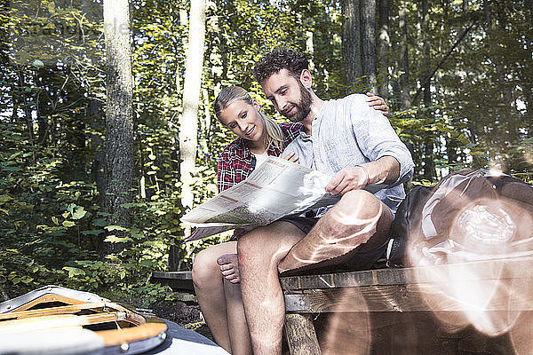 Junges Paar mit Karte und Kanu auf einem Steg an einem Waldbach sitzend