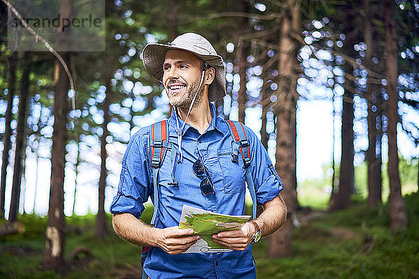 Lächelnder Mann mit einer Karte in der Hand wandert im Wald