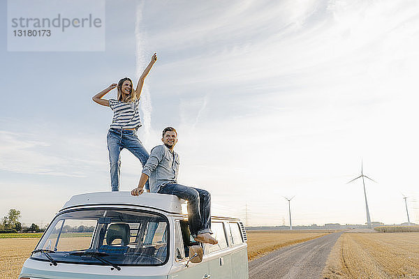 Glückliches Paar auf dem Dach eines Wohnmobils in ländlicher Landschaft