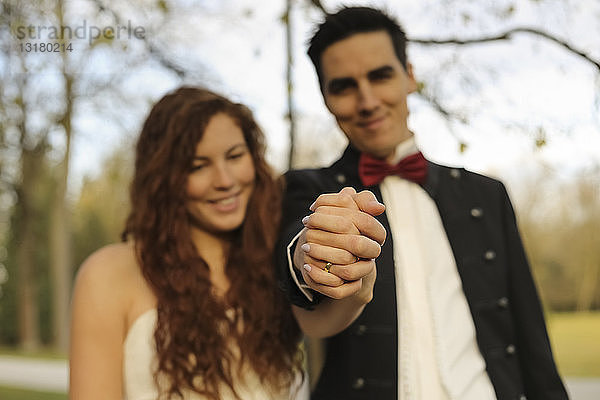 Glückliches Brautpaar steht im Park  hält Hände  zeigt Ehering