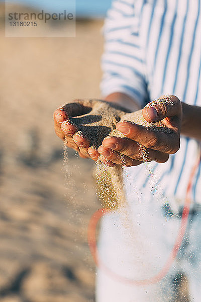 Frau am Strand  die Sand durch ihre Hände rieseln lässt  Nahaufnahme
