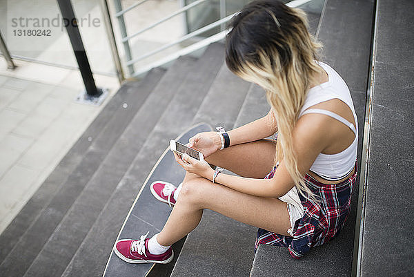 Junge Frau sitzt auf einer Treppe und benutzt ein Smartphone