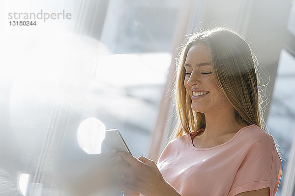 Porträt einer lachenden jungen Frau  die auf ein Handy schaut