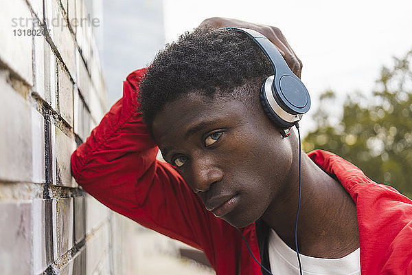 Junger schwarzer Mann lehnt an der Wand und hört Musik mit Kopfhörern
