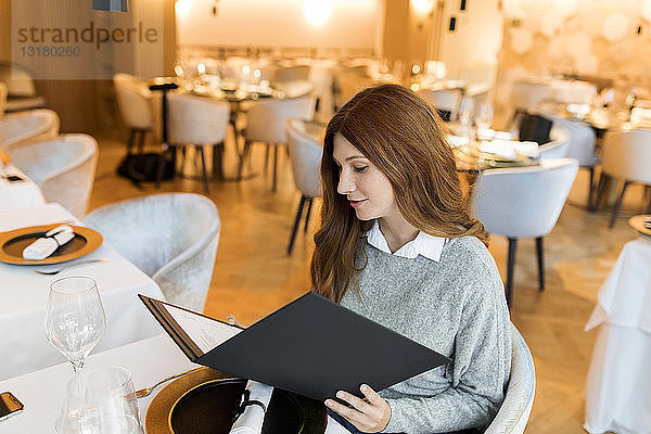 Frau  die in einem Restaurant am Tisch sitzt und die Speisekarte liest