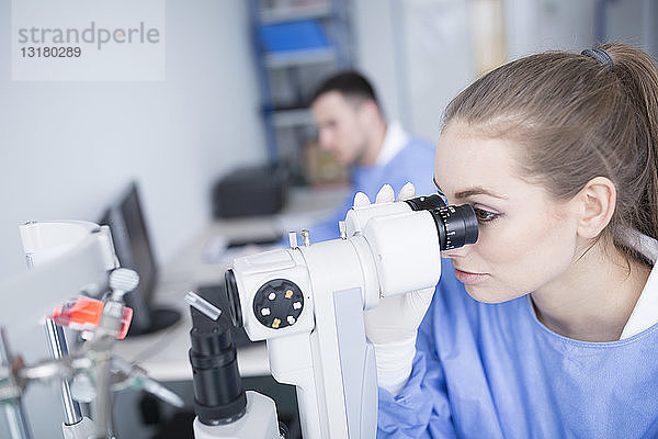 Laborant  der durch ein Mikroskop schaut