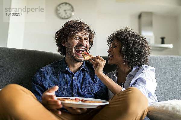 Glückliches Paar sitzt auf der Couch und isst Pizza