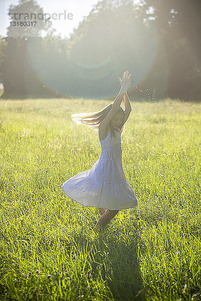 Glückliches Mädchen tanzt bei Gegenlicht auf der Sommerwiese
