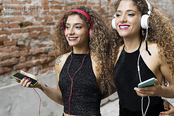 Porträt von glücklichen Zwillingsschwestern  die mit Kopfhörern und Mobiltelefonen Musik hören