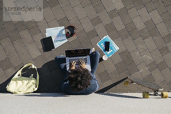 Junger Geschäftsmann sitzt im Freien an einer Wand und arbeitet am Laptop