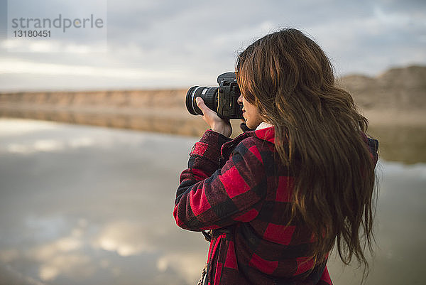 Junge Frau beim Fotografieren mit Kamera am Strand