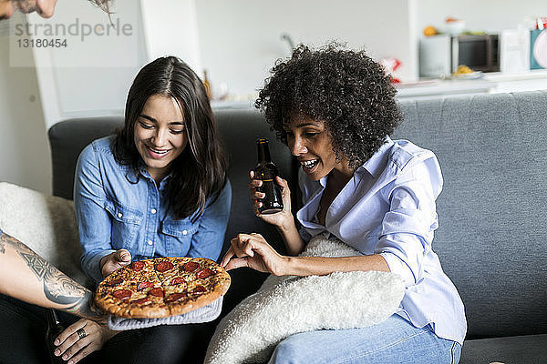 Tätowierter Mann bietet Freunden  die auf der Couch sitzen  Pizza an