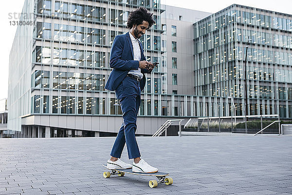 Spanien  Barcelona  junger Geschäftsmann fährt Skateboard und benutzt sein Handy in der Stadt