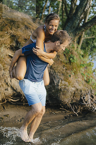 Glücklicher Mann trägt seine Freundin huckepack an einem See