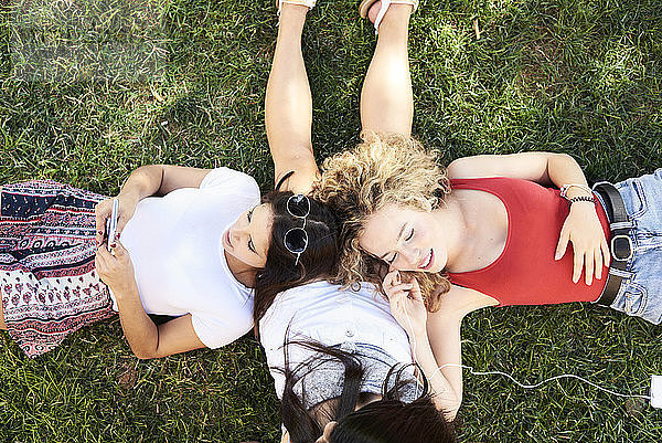 Drei junge Frauen liegen im Gras  telefonieren mit dem Handy und hören Musik