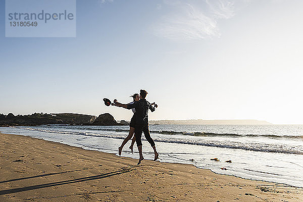 Frankreich  Bretagne  glückliches junges Paar springt bei Sonnenuntergang an den Strand