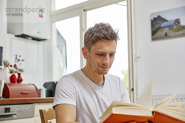 Lächelnder junger Mann liest zu Hause ein Buch