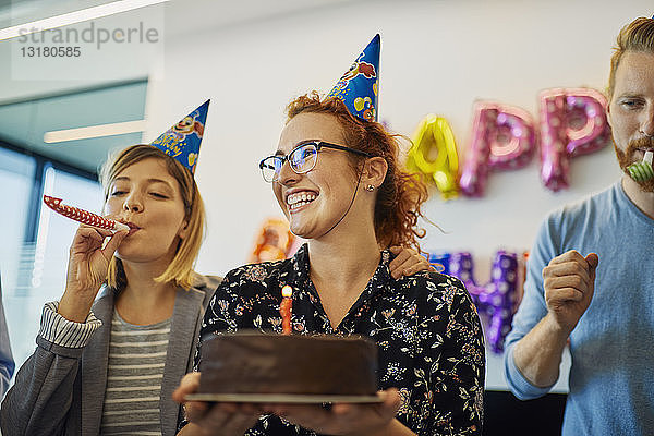 Kollegen mit einer Geburtstagsfeier im Büro mit Kuchen  Partyblower und Partyhüten
