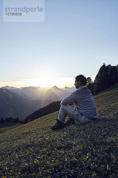 Österreich  Tirol  Rofangebirge  Wanderer bei Sonnenuntergang auf der Wiese sitzend