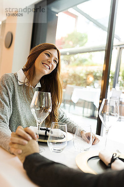 Lächelnde Frau hält in einem Restaurant mit einem Mann Händchen