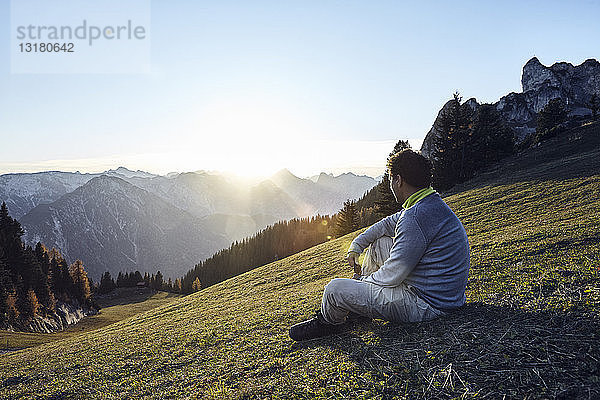 Österreich  Tirol  Rofangebirge  Wanderer bei Sonnenuntergang auf der Wiese sitzend