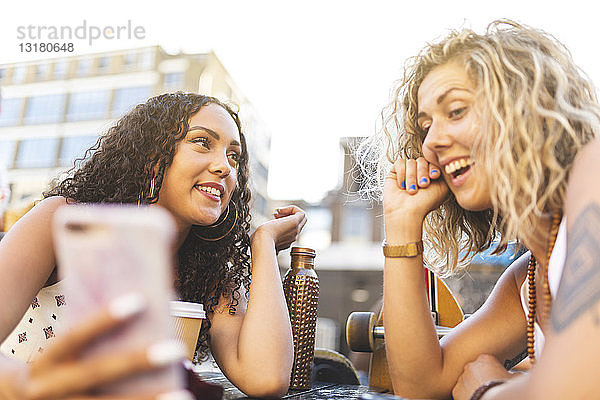 Zwei glückliche Freunde  die sich im Freien ein Handy teilen