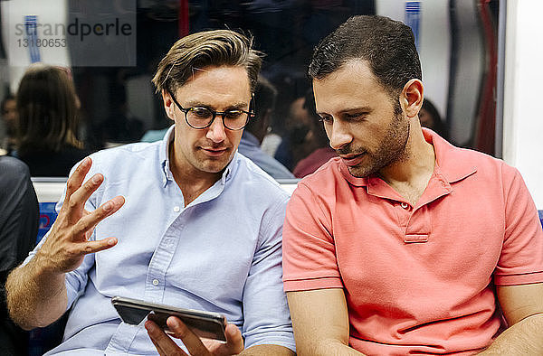 Porträt von zwei Freunden  die sich ein Handy in der U-Bahn teilen