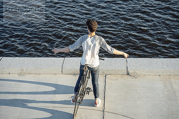 Junger Mann mit Pendler-Fixie-Fahrrad bei einer Pause am Flussufer