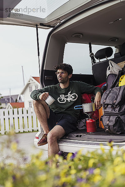 Junger Mann sitzt im Wohnwagen und bereitet Kaffee auf einem Campingkocher zu