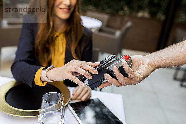 Frau  die in einem Restaurant mit einem Smartphone bezahlt
