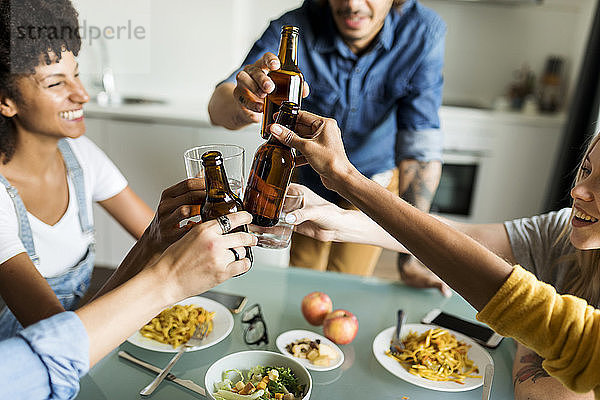 Fröhliche Freunde klirren mit Bierflaschen am Esstisch