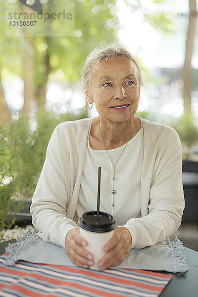 Lächelnde ältere Frau in einem Café im Freien mit seitlichem Blick