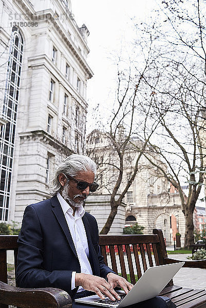 UK  London  leitender Geschäftsmann sitzt auf einer Bank im Freien und arbeitet am Laptop